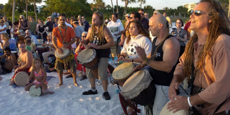 A lively drum circle on Siesta Key Beach with people joyfully playing drums together under the sun.