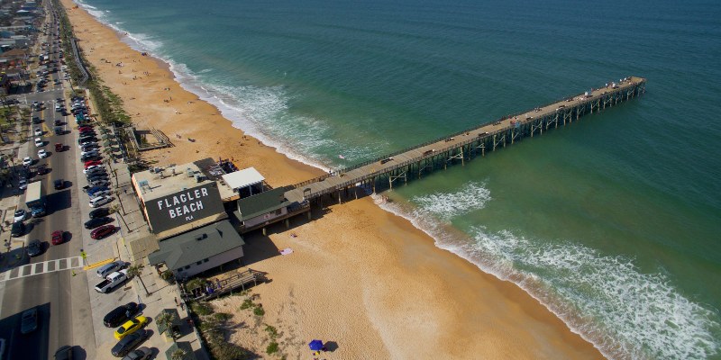 A view of a pier in Flagler Beach featuring parked cars, with the ocean visible in the background.