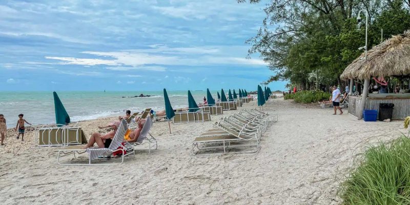 People lounging on the beach beside a thatched hut, enjoying the sun and the serene ocean view.