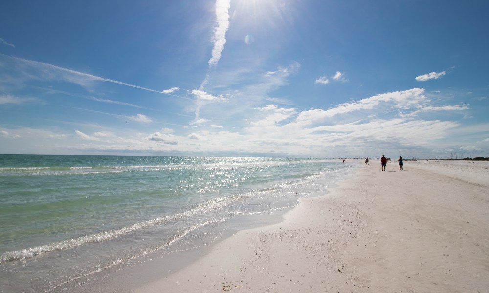 Sunlit Siesta Key Beach scene with people walking along the shore, embracing the warm weather and ocean views.