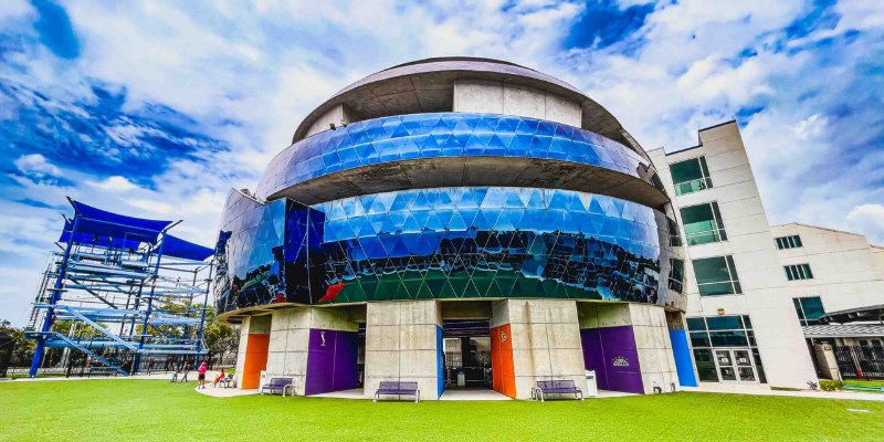 The Museum of Science and Industry features a colorful glass facade and a green grassy space in front.