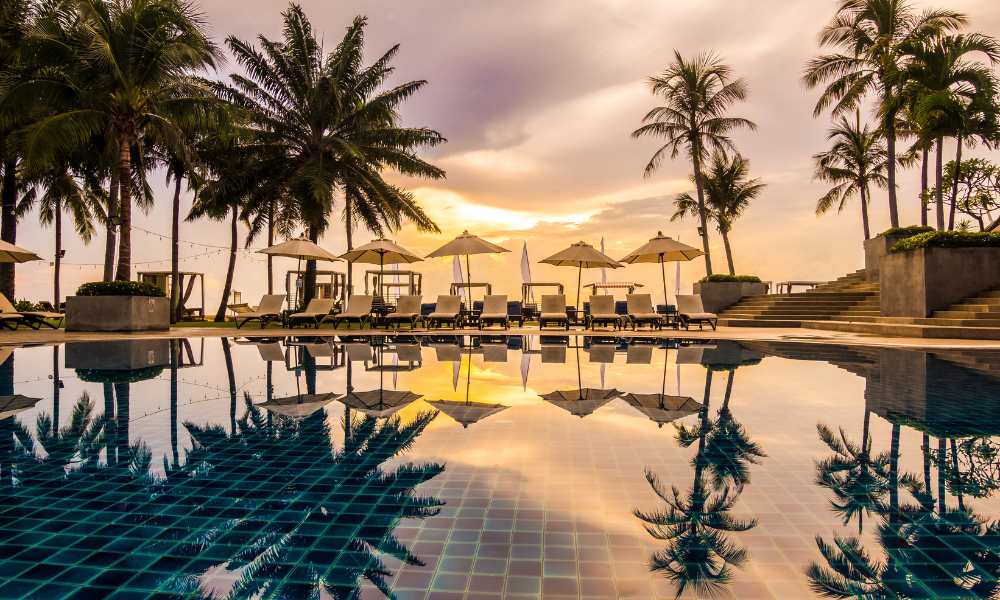 A serene swimming pool surrounded by palm trees, overlooking the beach at a luxurious resort.