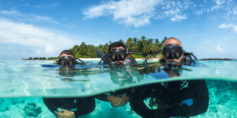 Three scuba divers explore clear waters with a tropical island visible in the background at Fort Zachary Taylor State Park.