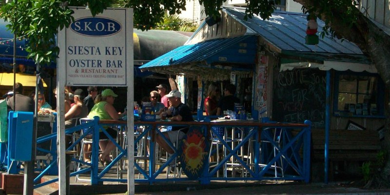 Outdoor dining scene at Siesta Key Oyster Bar with patrons enjoying their meals and a sign reading "SKOB"