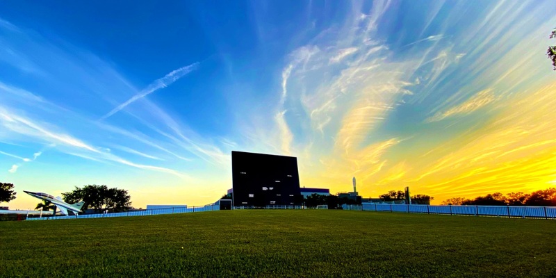 Sunset over a grassy field with the Space Mirror Memorial at Kennedy Space Center in the background.