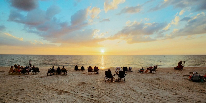 Sunset at Siesta Key Beach with people enjoying the view from their chairs and umbrellas.