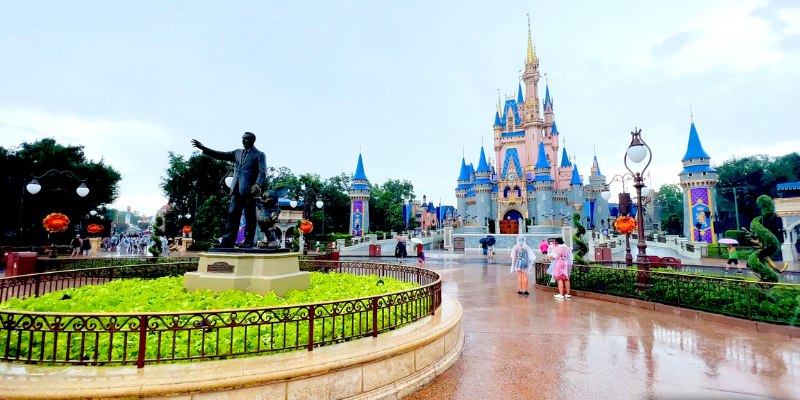 Disneyland under rain with a statue in front, showcasing the enchanting vibe of the park even on a gloomy day.