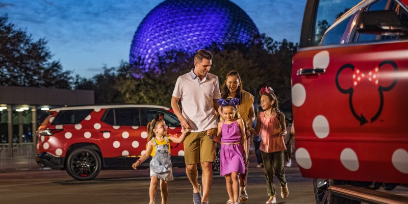 A family enjoys a day at Epcot, walking by a vibrant Minnie Mouse car at Walt Disney World.