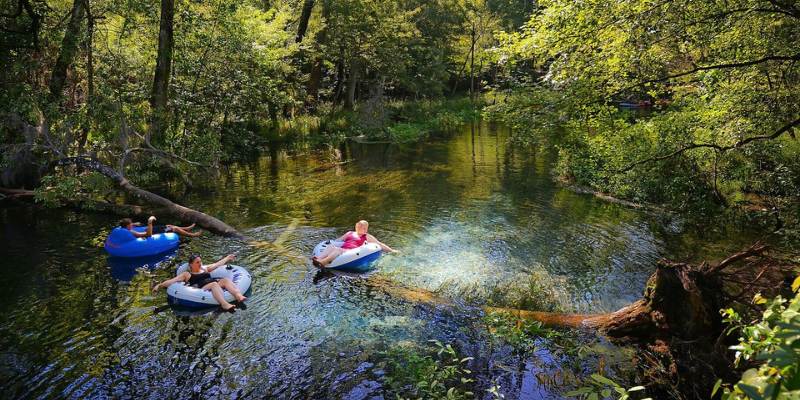 Three people in tubes enjoy kayaking down the Ichetucknee Springs River in Florida on a sunny day.