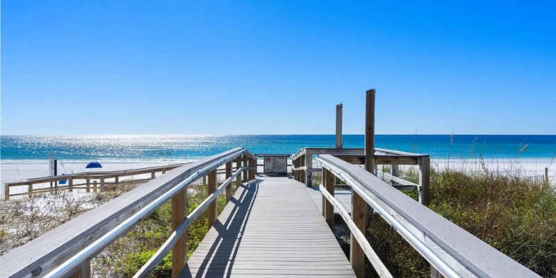 A wooden walkway leads through sand dunes to the sandy beach and blue ocean waves at Destin Beach.