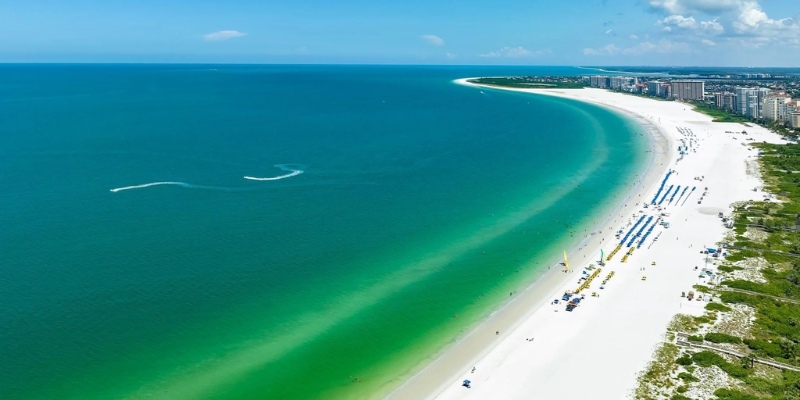 A view of Marco Island's beach, showcasing fine sand and tranquil ocean waves, with palm trees lining the background.