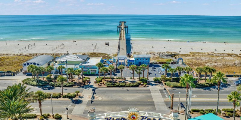 Bird's-eye view of Panama City Beach with soft sand and a wooden pier reaching out over the calm sea.