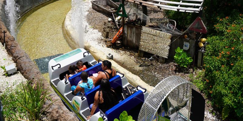 A group of people enjoying a water ride at Zoo Miami, smiling and raising their hands in excitement.
