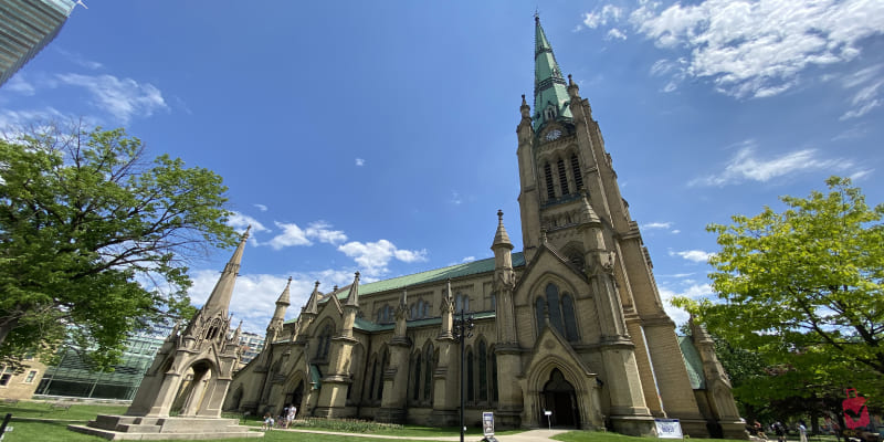 Low-angle of a historic Gothic church with a tall green steeple under a bright blue sky.