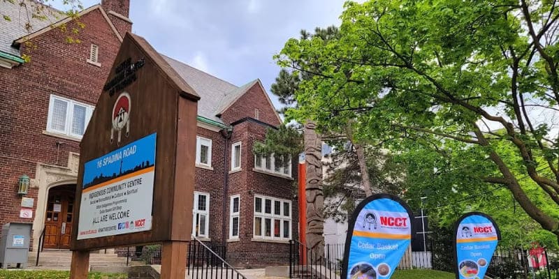 A brown brick building, the Native Canadian Centre of Toronto, with a large wooden sign and totem pole.