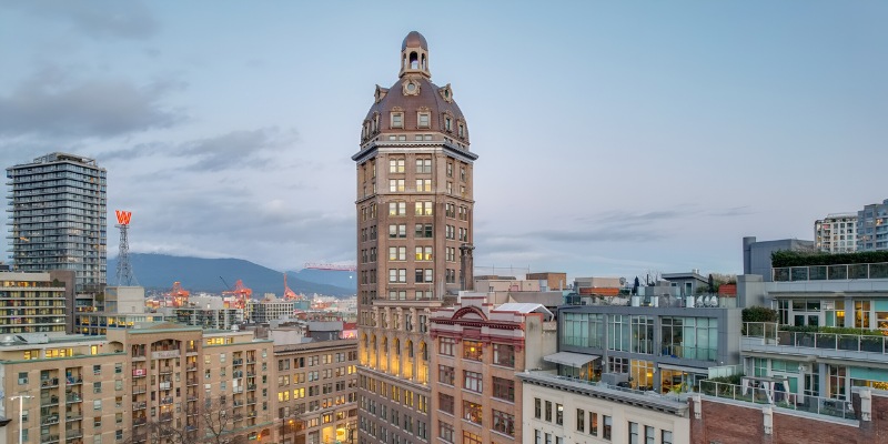 The Sun Tower, a historic building topped with a large copper dome and columned upper floors, rising above the surrounding urban rooftops under a cloudy sky.