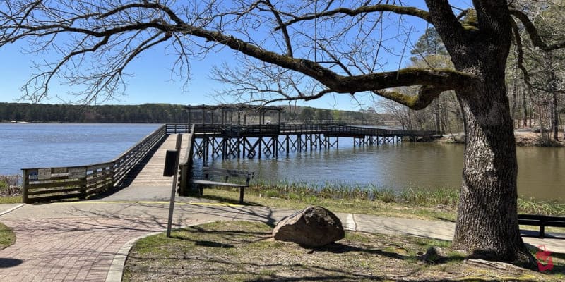 A truly beautiful day at Acworth Beach. A long, curving wooden pier gracefully extends over the calm lake, leading to a charming gazebo.