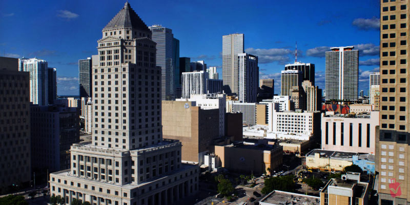 A skyline view of downtown Miami, highlighting the historic Dade County Courthouse among other tall buildings.
