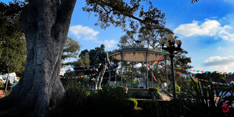 A statue stands in a park gazebo adorned with colorful flags, capturing the essence of El Pueblo de Los Angeles.