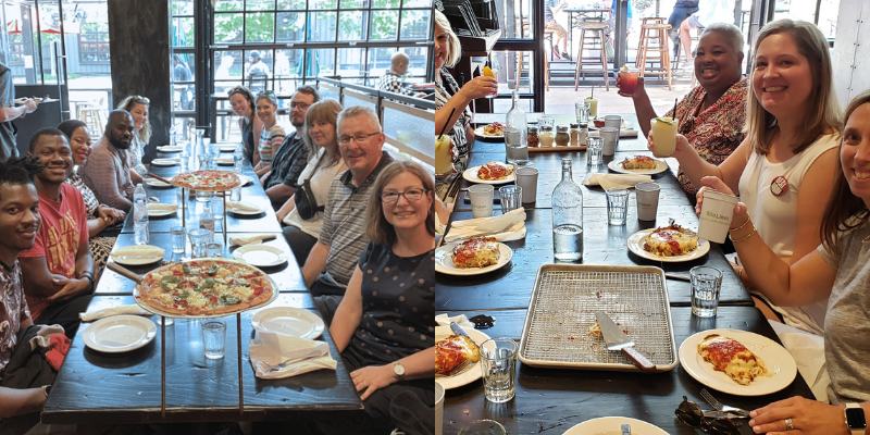 A large group of diverse people gathered around a long table in a restaurant, laughing and smiling while enjoying a food tour experience with pizza and other dishes, showcasing a convivial dining atmosphere.