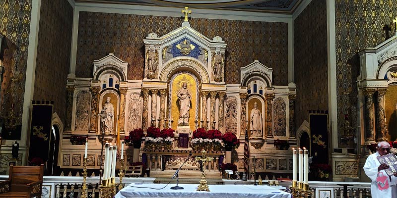The ornate altar of Gesu Church in Miami, decorated with statues, candles, and red flowers.