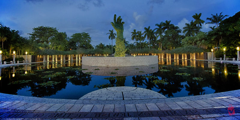 The Holocaust Memorial in Miami Beach, featuring a large hand sculpture rising from a reflective pool, surrounded by palm trees.