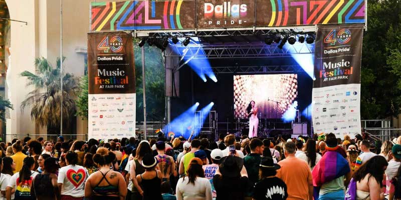 A singer performs on a stage decorated with rainbow banners for a crowd at Fair Park, representing the variety of musical festivals in Dallas.
