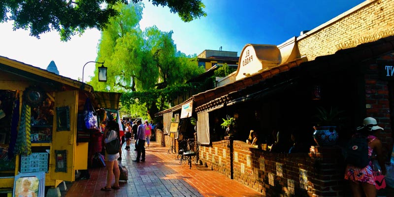Pedestrians stroll along a vibrant street lined with shops and restaurants, depicting the lively atmosphere of Olvera Street.