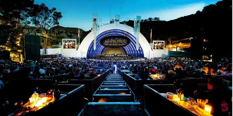 The Hollywood Bowl at dusk, featuring a crowded amphitheater with a symphony orchestra on stage, highlighting a famous music venue.