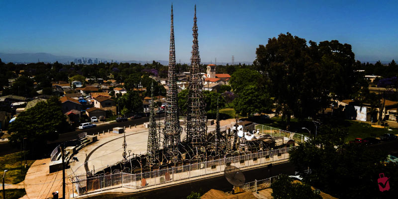 An aerial view of the Watts Towers, intricate sculptural towers rising above a residential neighborhood.