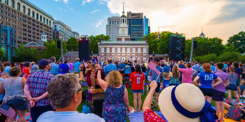 A large crowd gathers with American flags at Independence Hall, capturing the spirit of America 250 celebrations in Philadelphia.