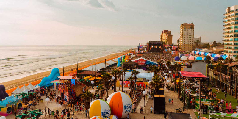 An aerial view of a vibrant beach music festival with multiple stages, large inflatable decorations, and many people.
