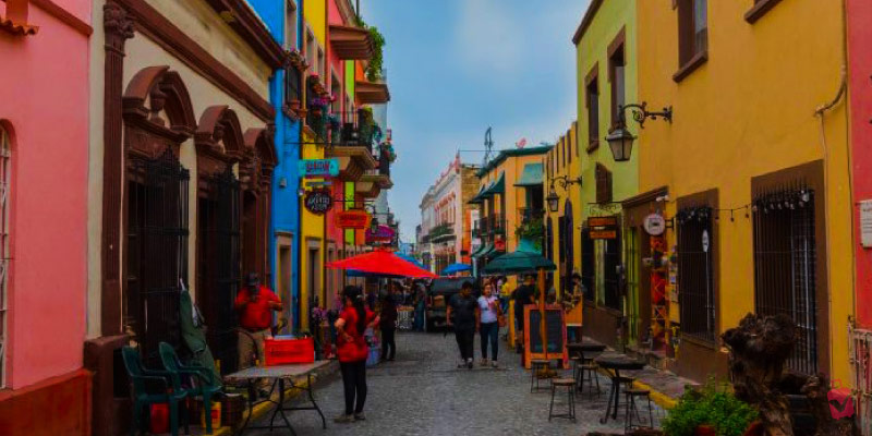 A vibrant street scene in Barrio Antiguo, Monterrey, Mexico, with colorful buildings, people, and outdoor seating under a bright sky.