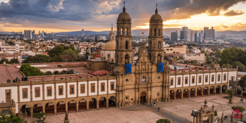 An aerial shot of the Basílica de Nuestra Señora de Zapopan, a large historic church near Guadalajara, with a grand plaza in front.