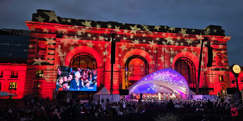A nighttime crowd enjoys an outdoor orchestra concert for Celebration at the Station with Union Station illuminated in red and white stars in Kansas City.