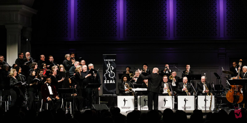 Musicians and a choir perform on stage at the Earshot Jazz Festival, with a conductor leading the ensemble.