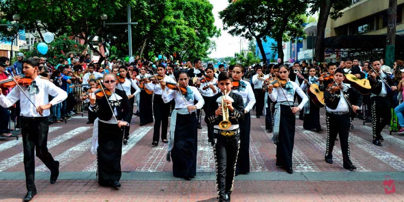 Youth mariachi band in traditional outfits playing violins and trumpets during a street parade at the Encuentro Internacional del Mariachi y la Charrería.