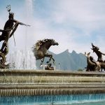 The Fuente de Neptuno fountain, a famous historical landmark in Monterrey, Mexico, with bronze statues of Neptune and horses spouting water, against a mountain backdrop.