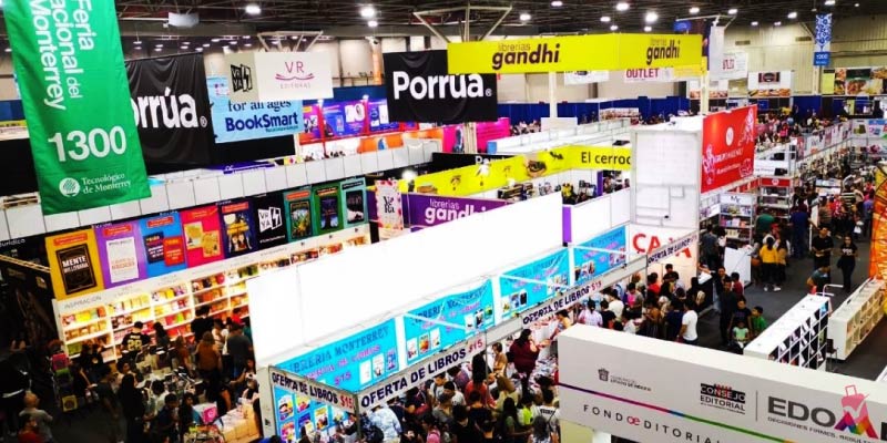 A bustling indoor book fair, the Feria Internacional del Libro Monterrey, with numerous stalls, banners, and crowds of people browsing books.