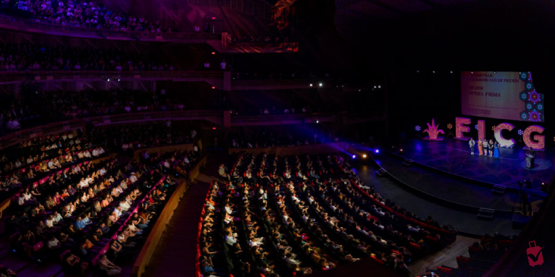 Large auditorium filled with people watching an awards ceremony at the Festival Internacional de Cine (FICG) on a stage with large lit letters.