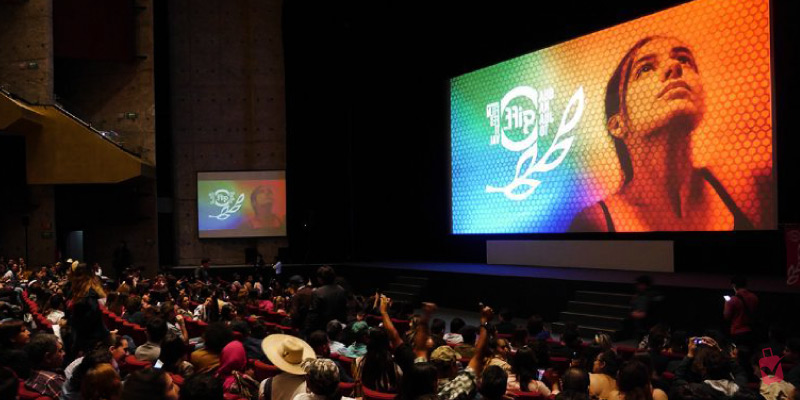 A large audience watches a film screening at the Festival Internacional de Cine Monterrey, with a vibrant, colorful image projected onto a large screen.