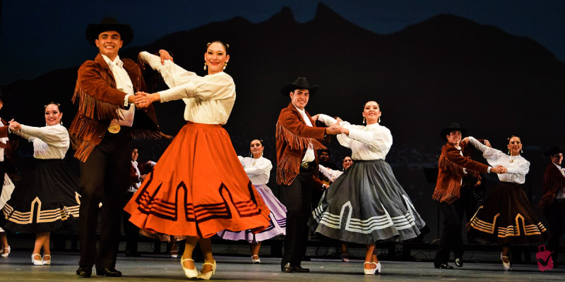 Dancers in traditional Mexican attire perform on stage, with men in sombreros and women in long, flowing skirts, at the Festival Internacional de Santa Lucía.