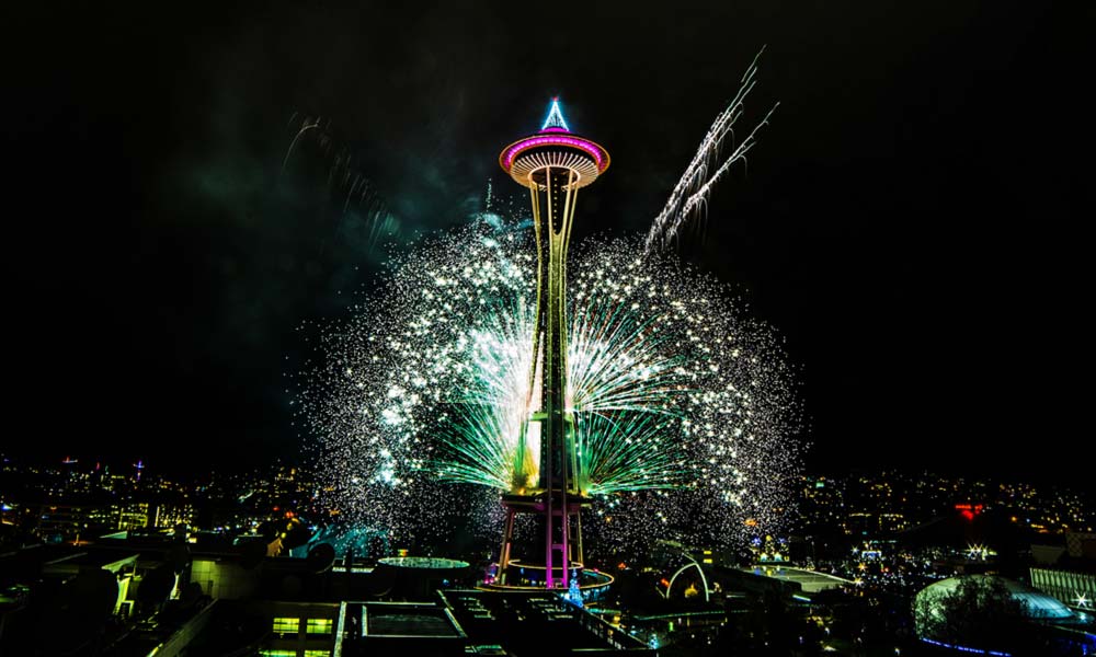 The Space Needle erupts with colorful fireworks against the night sky, celebrating a festival or event in Seattle.