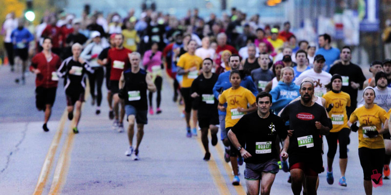 A dense pack of runners in colorful athletic gear with race bibs competes on city streets during the Garmin KC Marathon.