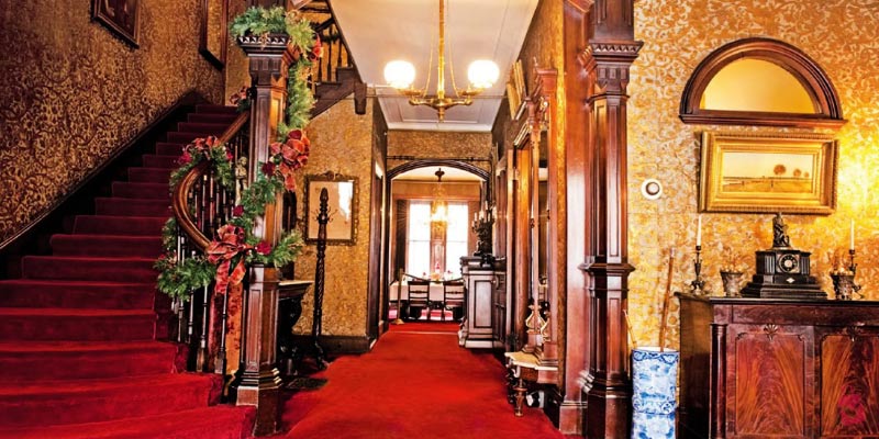 An elegant Victorian hallway with red carpet and a grand staircase showcases the well-preserved historic interior of the gibson house museum in boston.