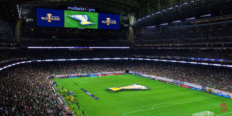 A massive crowd fills the stands of a premier houston stadium for a major international soccer match under bright arena lights.