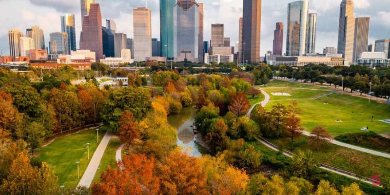 Lush green trees and a winding river in a city park under a bright sky showcase the vibrant outdoor environment typical of houston summer weather.