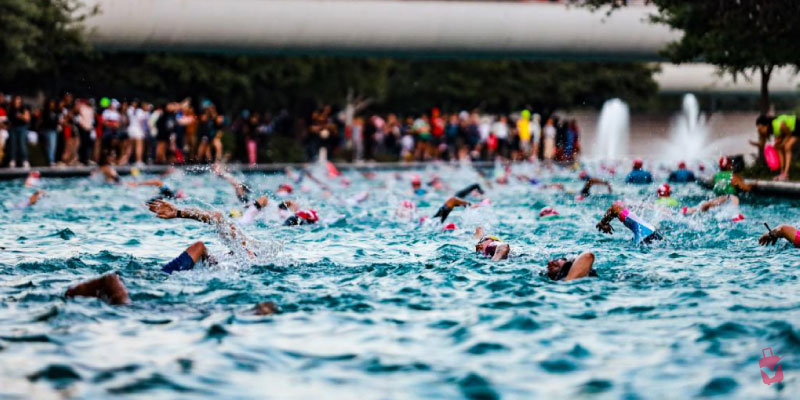 Swimmers compete in open water during the Ironman 70.3 Monterrey, with many arms splashing and faces visible in the water.