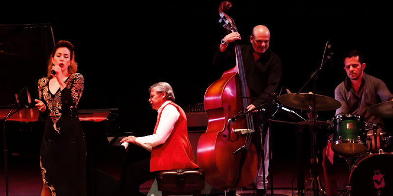 A jazz quartet featuring a singer, pianist, double bassist, and drummer performs on a dark stage during the Jalisco Jazz Festival in Guadalajara.