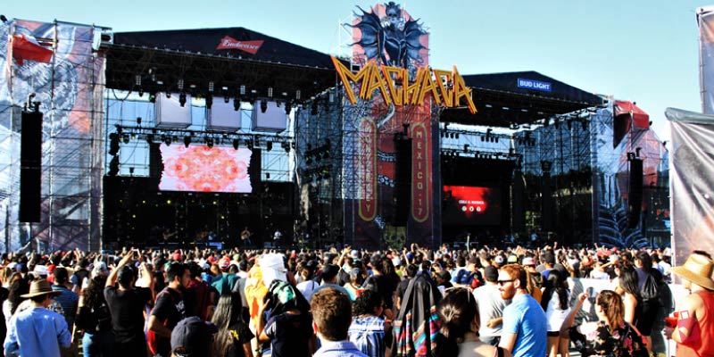 A large music festival crowd faces a massive stage with multiple screens and elaborate lighting, displaying the Machaca Fest logo.